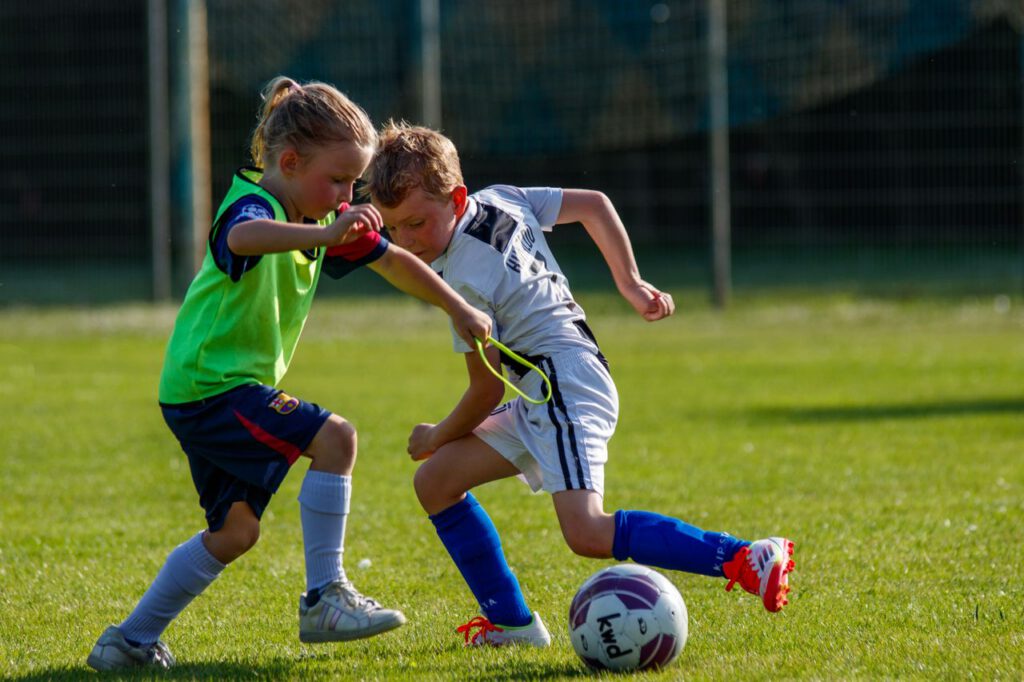 Two kids playing soccer on a sunny day, showcasing teamwork and sportsmanship.