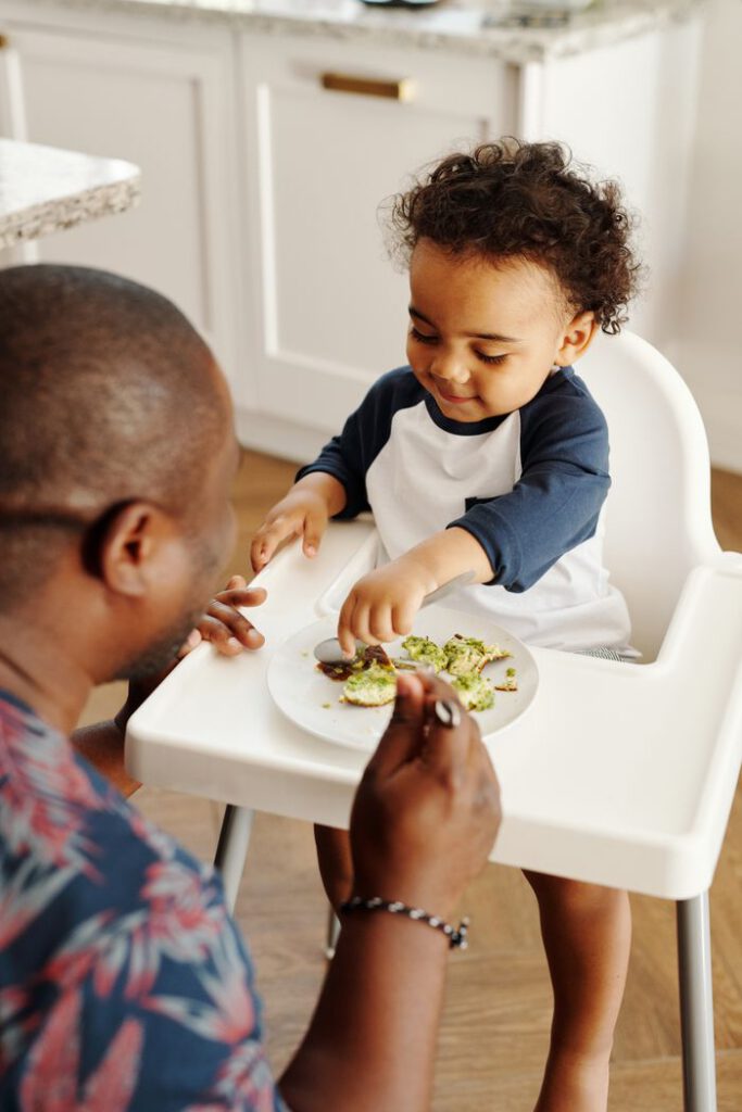 A heartwarming moment of a father feeding his son breakfast in a high chair.