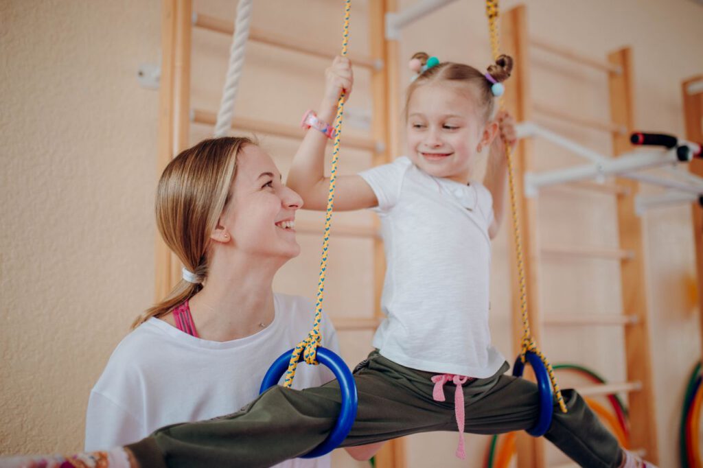 pexels photo 7427558 Smiling mother teaches her daughter gymnastics on rings indoors, fostering bonding and flexibility.